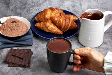Woman holding a cup of hot chocolate next to some delicious croissants and various toppings