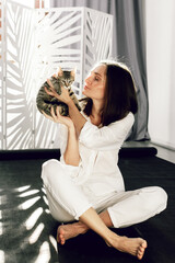 In the sunlight, a young woman in a white shirt holds a gray kitten in her arms.