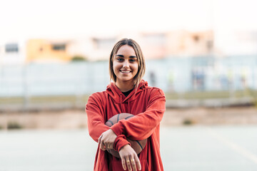 Smiling young woman in sportswear holding a basketball outdoors