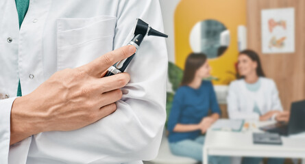 Audiologist with otoscope over background consultation doctor with patient at hearing clinic. Ear...