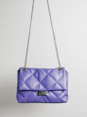Quilted crossbody bag in violet very peri color with metal chain strap on neutral light background....