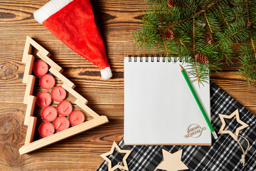 Wooden christmas tree with red candles inside, with santa hat, fir branches, pine cones and wooden stars with blank notebook