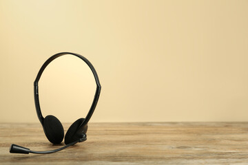 Headset on wooden table against beige background, space for text
