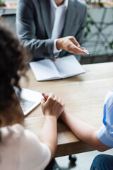 cropped view of realtor pointing with pen near empty notebook and interracial lesbian couple holding hands on blurred foreground