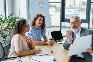 middle aged realtor showing document to multiethnic lesbian couple in real estate agency