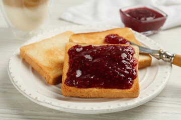 Toast with tasty raspberry jam and roasted slices of bread on white wooden table, closeup