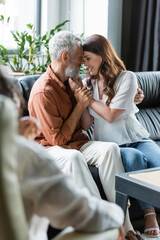pleased couple embracing on sofa near blurred african american psychologist in consulting room