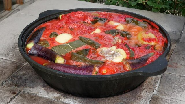 Large caldron with stuffed vegetables in tomato sauce on open fire. Cooking dinner outdoors