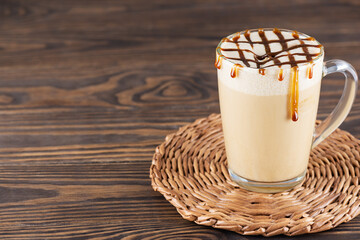 Caramel latte macchiato in a glass mug on a wooden table. Horizontal orientation, copy space.