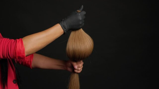 Preparation for hair extension. Girl holding hair in her hand on a black background close-up.