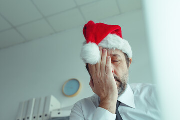 Pessimistic businessman with Santa Claus hat suffering from Christmas holiday season depression