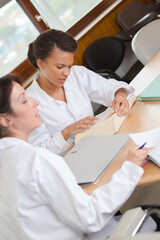 Obraz premium Women in white jackets studying at desk