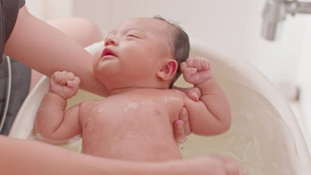 Calm of asian newborn baby bathing in bathtub.mother bathing her son in warm water.adorable newborn infant smile in tub relax and comfortable.Newborn baby care concept