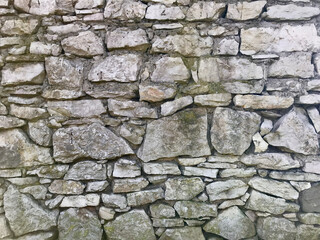 Old medieval stone wall along a street. Photo closeup of aged building made of grey stone masonry  outside on cityscape background. Horizontal seamless pattern. Stone fence texture for the background.