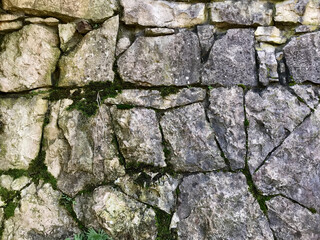 Old medieval stone wall along a street. Photo closeup of aged building made of grey stone masonry  outside on cityscape background. Horizontal seamless pattern. Stone fence texture for the background.