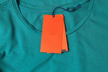Blank orange tags on pale green t-shirt, top view. Space for text