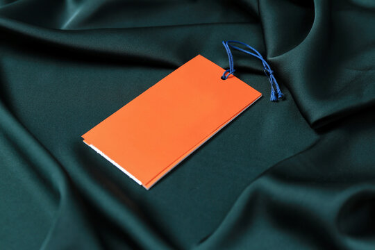 Blank orange tags on green silky fabric, closeup. Space for text