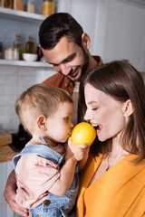 Woman biting lemon near toddler son and husband at home