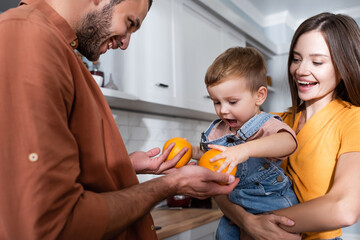 Man holding oranges near kid and wife at home