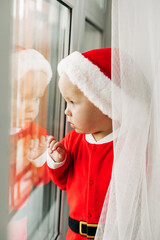A kid in a New Year's costume is waiting at the Christmas window. Christmas, waiting for the holiday, magic