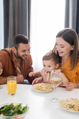 Positive parents looking at son eating pasta at home