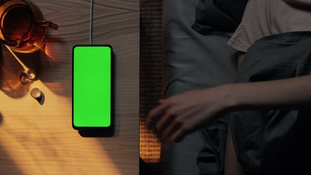 Woman in bed tapping on charging mobile with green screen