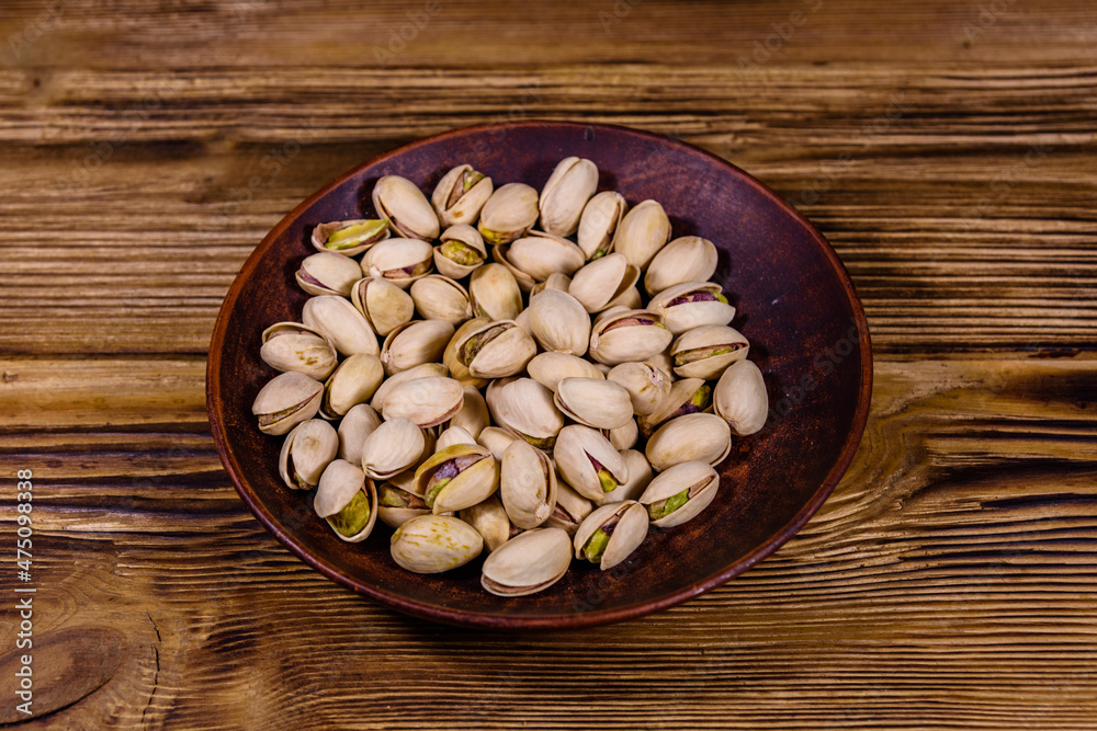 Wall mural Ceramic plate with pistachio nuts on a wooden table - Wall murals