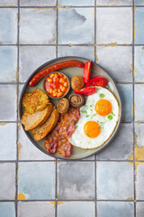 English Breakfast with fried eggs, sausages, bacon, beans, toasts, tomatoes and mushrooms tile background.
