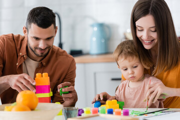 Smiling woman drawing near son and husband with building blocks at home