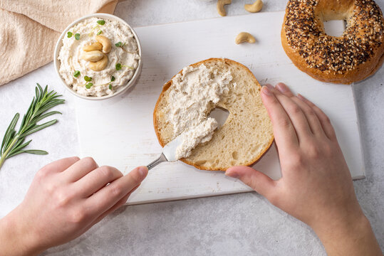 Female Hands Spreading Cashew Cheese On A Bagel.