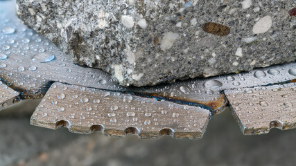 Close-up of saw blade diamond segments with water drops and piece of a gray tile. Sharp steel...