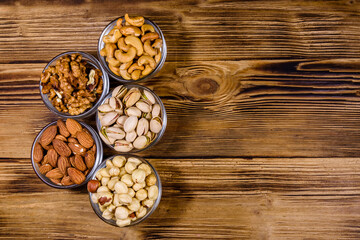 Obraz na płótnie Canvas Various nuts (almond, cashew, hazelnut, pistachio, walnut) in glass bowls on a wooden table. Vegetarian meal. Healthy eating concept. Top view