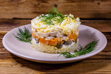Salad with chicken breast, marinated mushrooms, carrot, eggs, boiled potato and mayonnaise on a wooden table