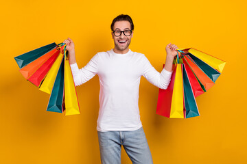 Photo of nice brunet millennial guy hold bags wear eyewear white outfit isolated on vibrant yellow color background