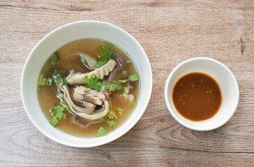 boiled slice pork stomach and bone soup in bowl dipping spicy sauce cup on table