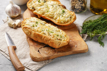Two halves of garlic and butter bread - baguette on a wooden board, sea salt, pepper, dill and garlic cloves on a grey concrete background, top view