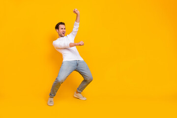 Full size photo of cool brunet young guy ride hourse wear white shirt jeans sneakers isolated on yellow color background