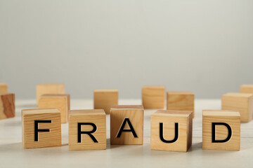 Wooden cubes with word Fraud on white table, space for text