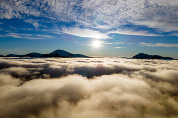 Aerial view of vibrant sunrise over white dense clouds with distant dark mountains on horizon