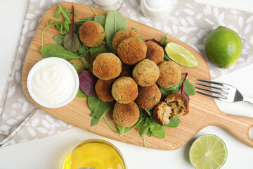 Delicious falafel balls with herbs, lime and sauce on white wooden table, flat lay