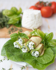 Ricotta cheese mixed with herbs in a zucchini roll lies on lettuce leaves.