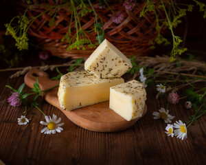 Caciotta cheese lies on a wooden board with wildflowers and hay in the background.