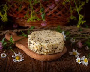 Caciotta cheese lies on a wooden board with wildflowers and hay in the background.