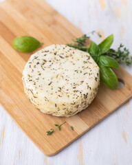 Caciotta cheese lies on a wooden board with basil and thyme.