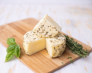 Caciotta cheese lies on a wooden board with basil and thyme.