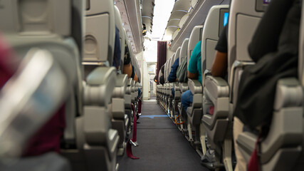 Obraz premium passenger seat, Interior of airplane with passengers sitting on seats and stewardess walking the aisle in background.