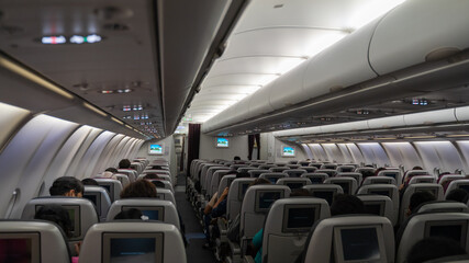 passenger seat, Interior of airplane with passengers sitting on seats and stewardess walking the aisle in background.