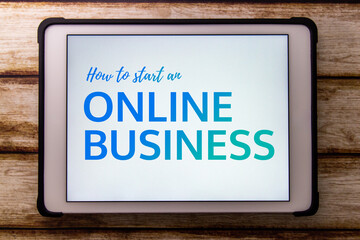 Conceptual keyword “How to Start an Online Business” on tablet on faded shabby table. Online...