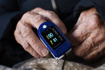 Digital finger oximeter on hand of an elderly woman. Monitoring of pulse and blood oxygen levels at...