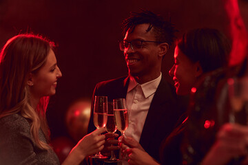 Group of elegant young people drinking champagne in while enjoying party in nightclub or restaurant